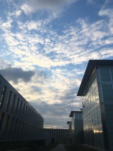 A bright blue sky partially obscured by elongated clouds, with glass and steel buildings in the foreground